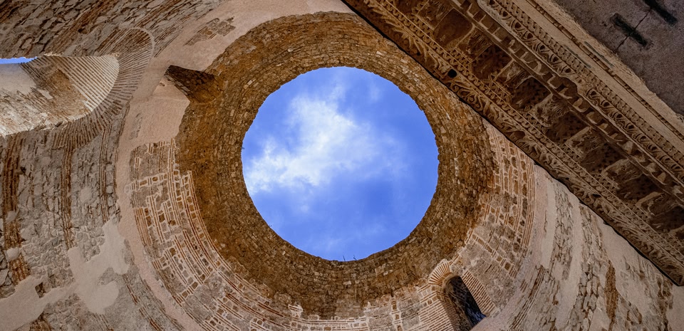 Vue vers le ciel à travers l'oculus d'une ruine antique aux murs de pierre sculptée.