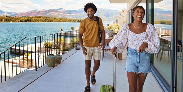 Man and woman walking into their holiday accommodation with their suitcase and rucksack.