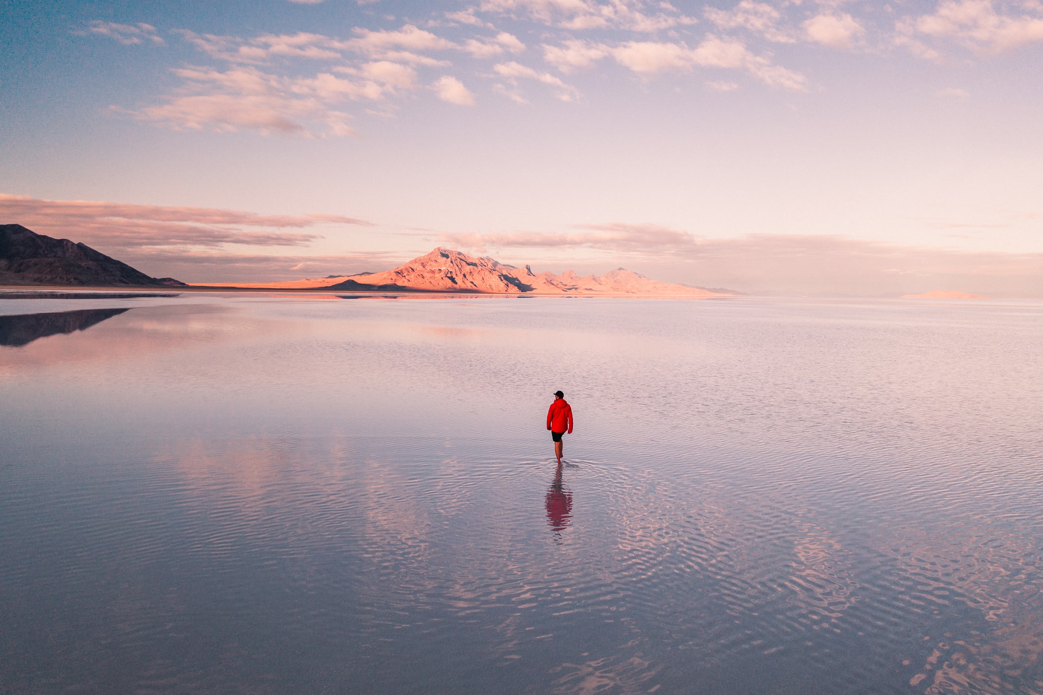 Traveller in the distance walking on the water with mountains in the background. Clouds and pink sky.
