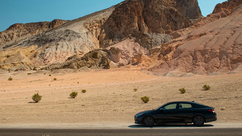 Black car parked on a desert road with colorful mountains in the background. Travel photography, scenic drive, road trip.