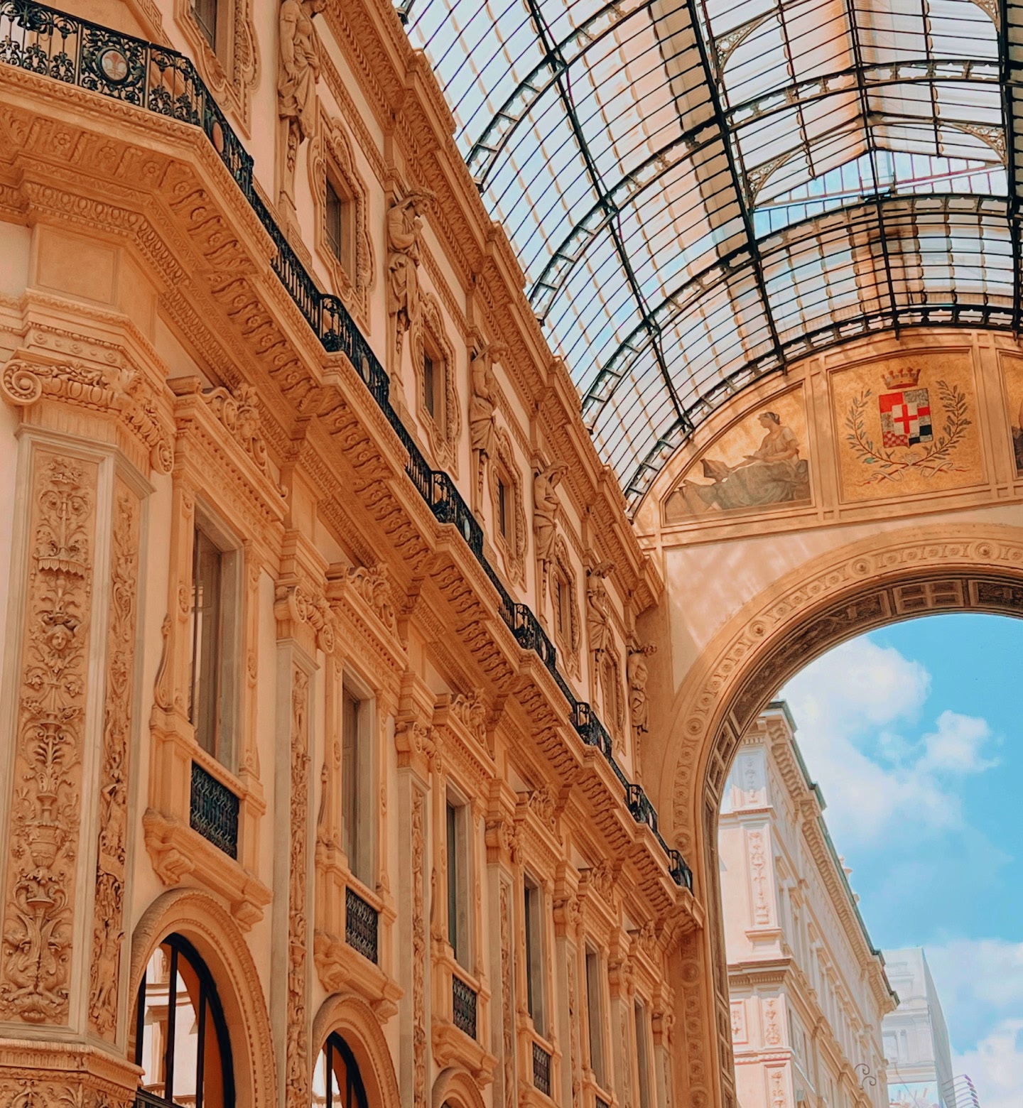 Sunlight filters through a glass roof over an ornate Milan shopping arcade.
