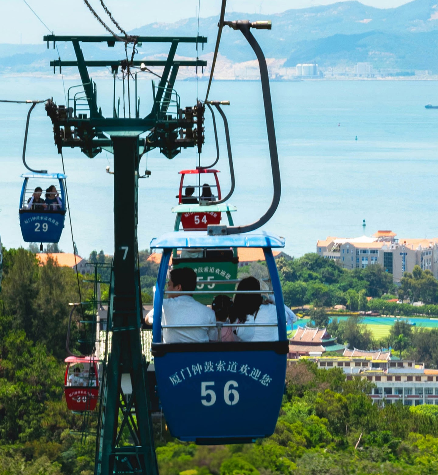 Colourful cable cars glide above green hills and blue coastline in Xiamen, China.