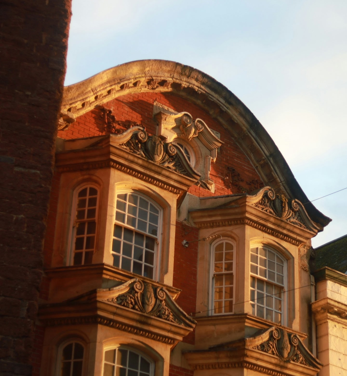 Gouden zonlicht dat sierlijke ramen raakt op een rood bakstenen gebouw in Exeter, VK.