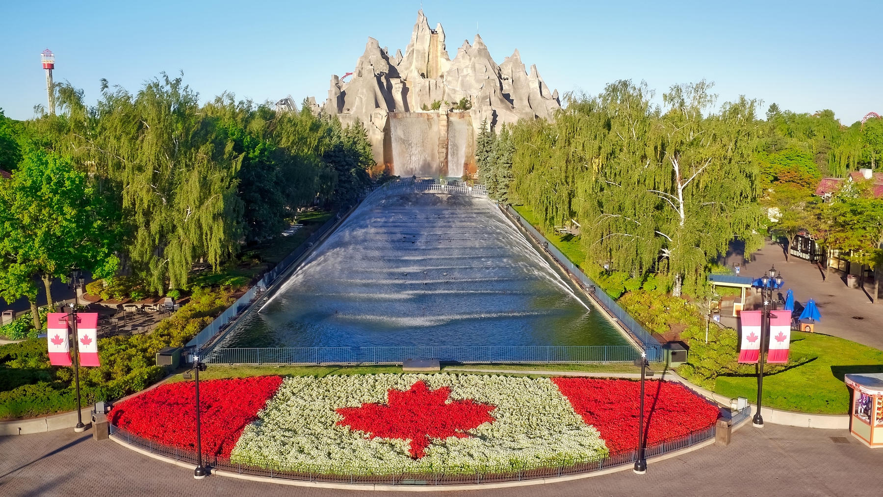 Canada flag made out of flowers with trees and a water feature in the background