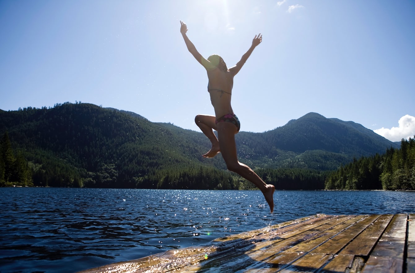 person happily jumping into the water in the Okanagan Lake on a sunny summer day.