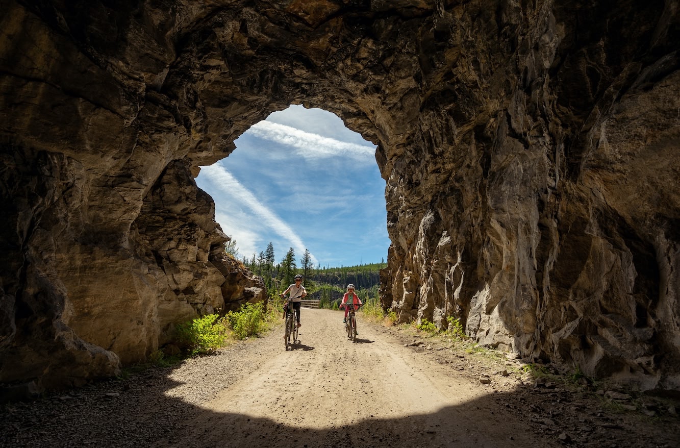 two people cycling through a tunnel in Myra Canyon, a top adventure activity and thing to do near Kelowna, BC.
