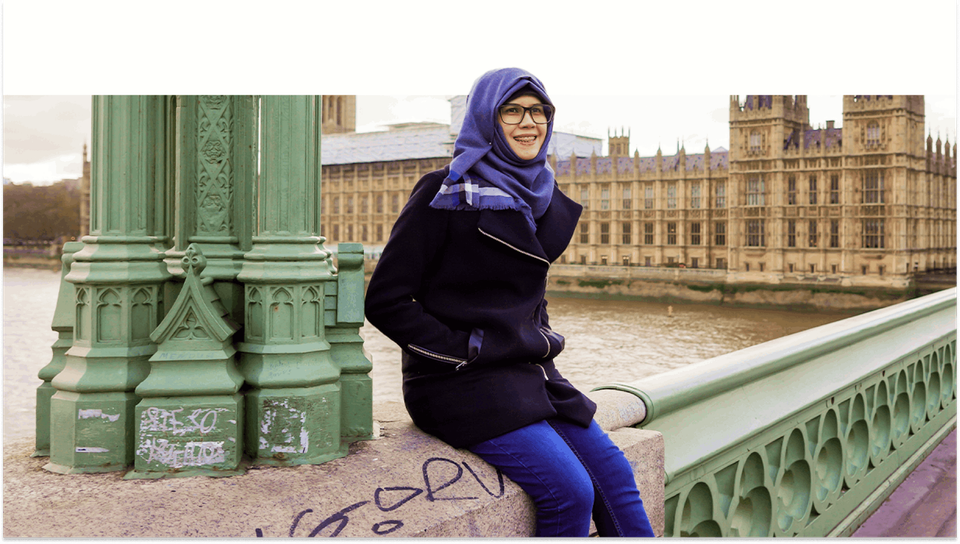 A joyful woman sitting at the picturesque edge of Westminster Bridge, her radiant smile complementing the iconic backdrop of the Houses of Parliament in the distance.