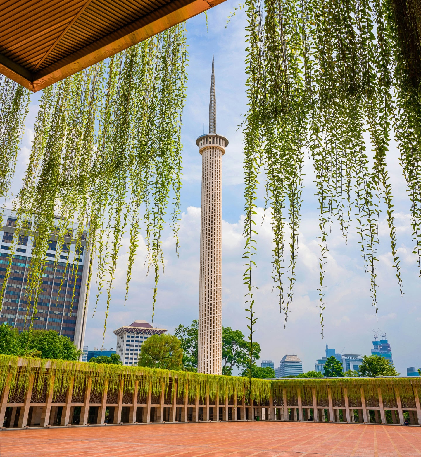 Un'alta guglia incorniciata da rampicanti verdi con un paesaggio urbano di Giacarta, in Indonesia.