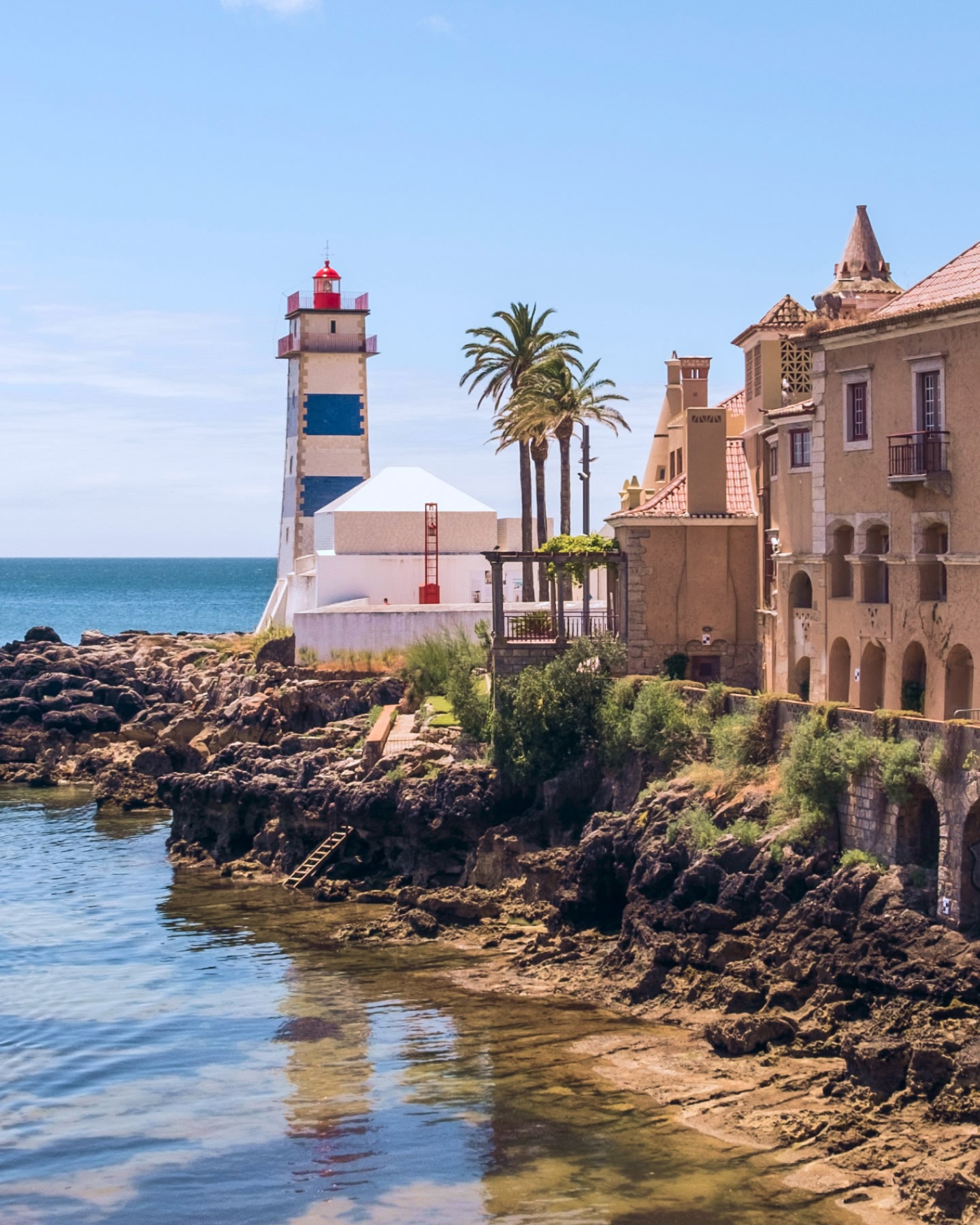 Un phare rouge, bleu et blanc se dressant près d'un rivage rocheux et de bâtiments anciens à Cascais, au Portugal.