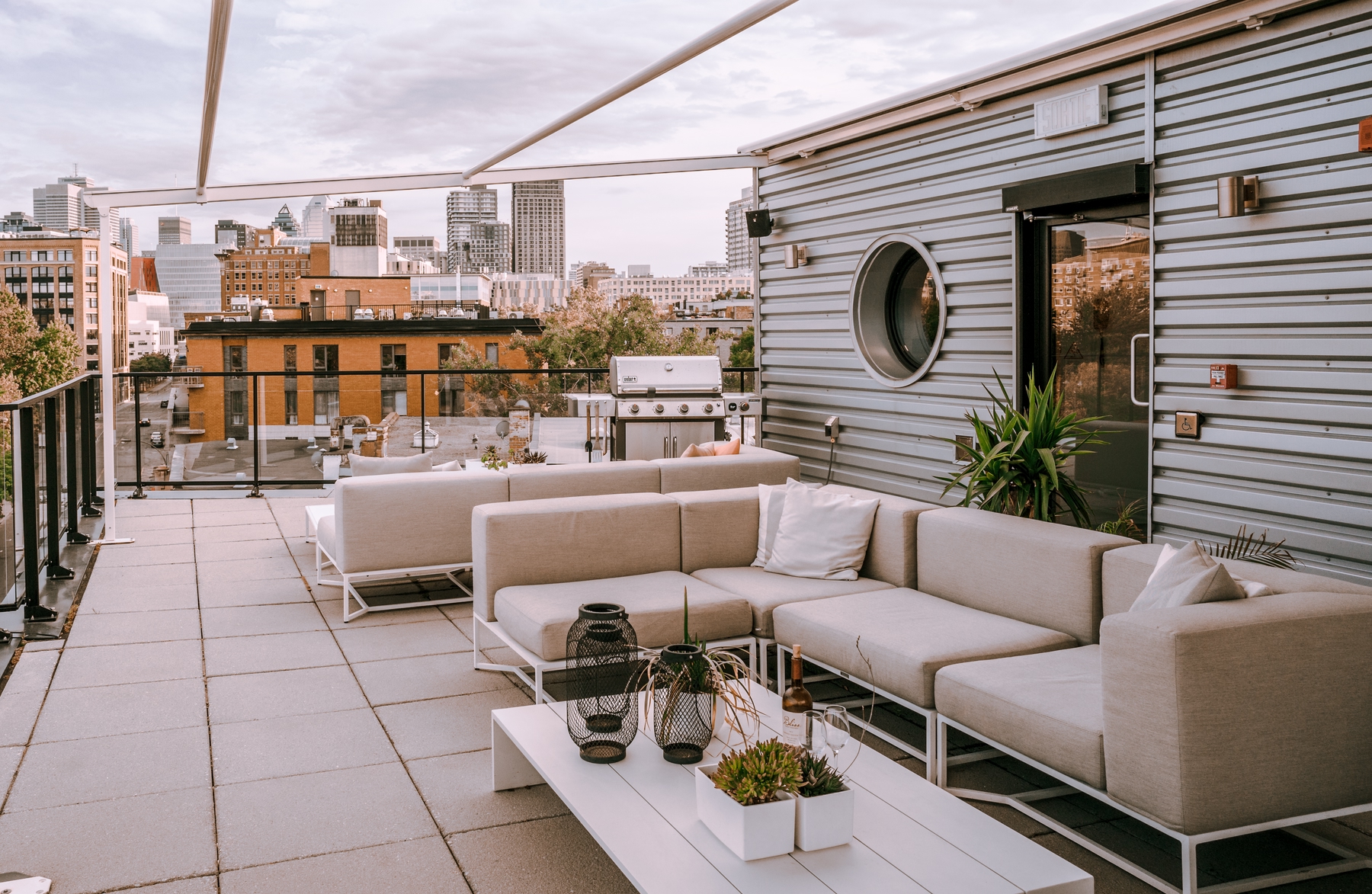 Rooftop at Boxotel, eco-friendly boutique hotel in Montreal. White couches, tables, and Montreal skyline in the background