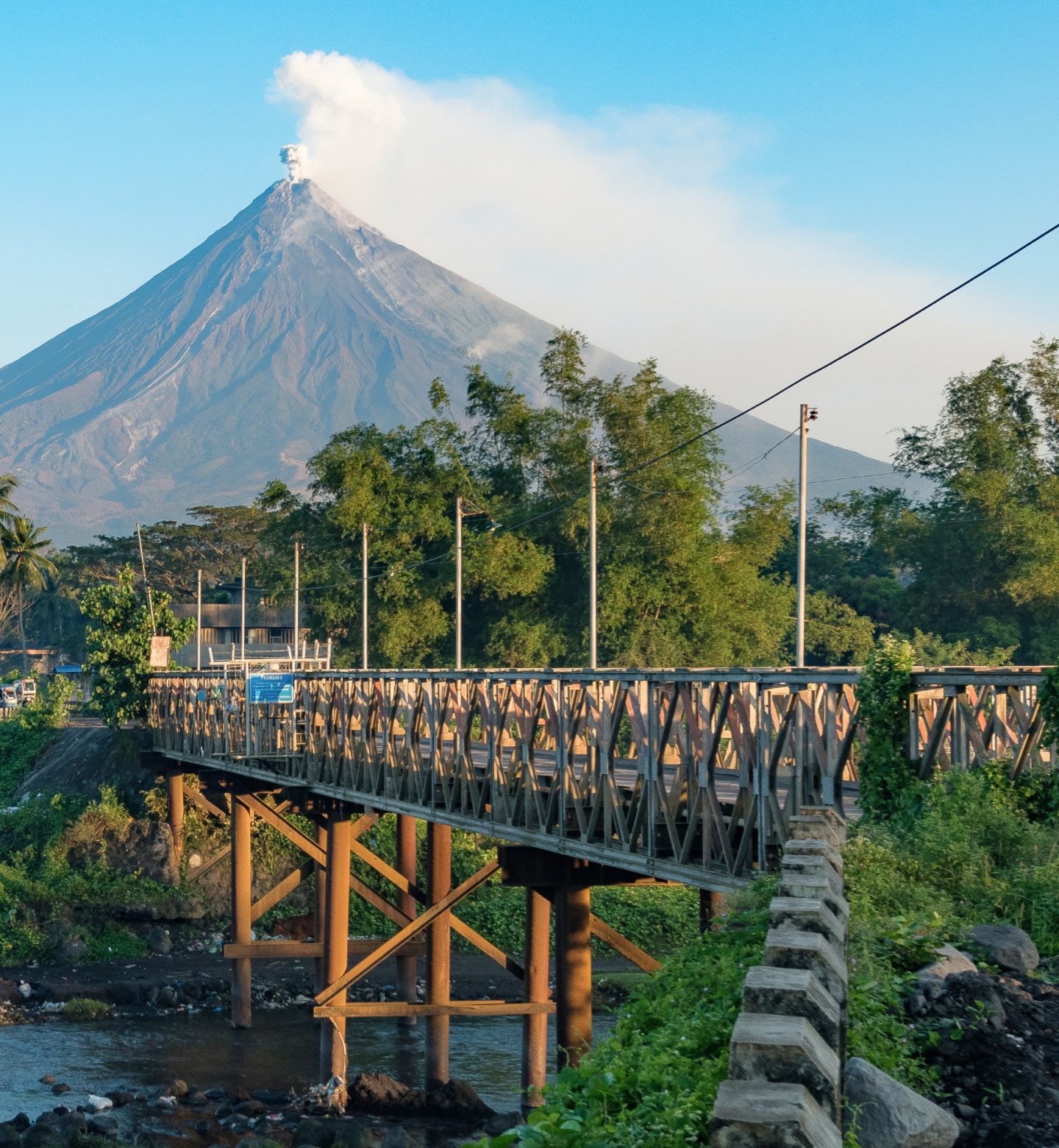 Un volcan émet de la fumée au-dessus d'arbres verts et d'un pont en bois à Legazpi, aux Philippines.