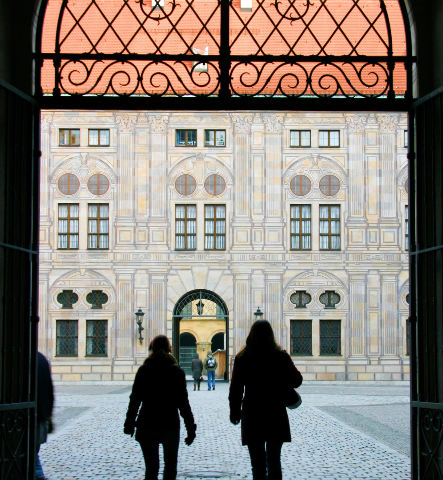 Two people silhouetted from behind as they walk through a cobbled courtyard in Munich, Germany.