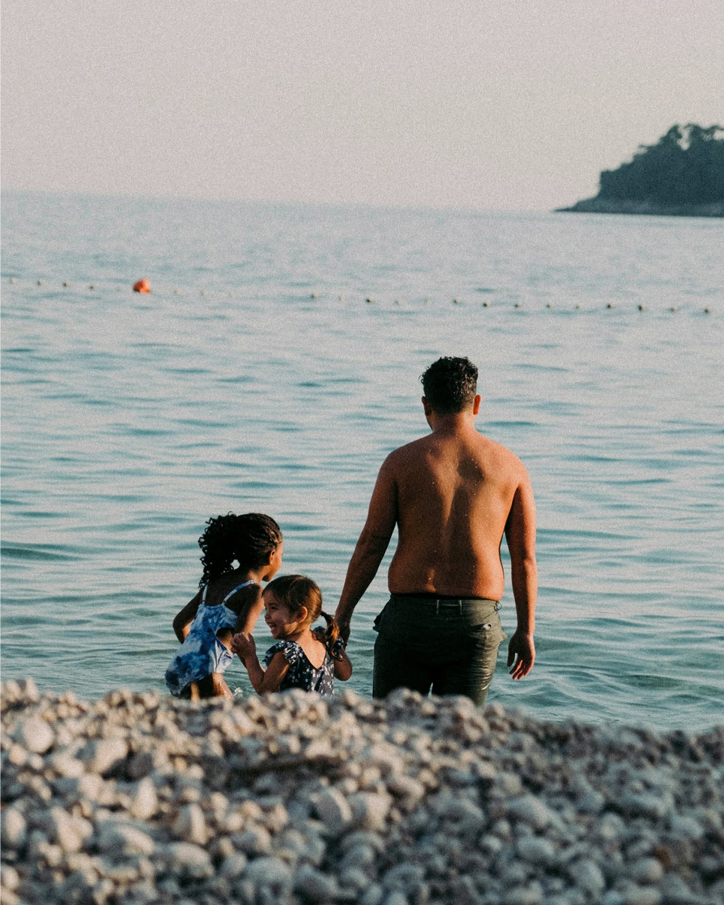 Un padre y sus dos hijas pequeñas entran al mar desde una playa de guijarros.