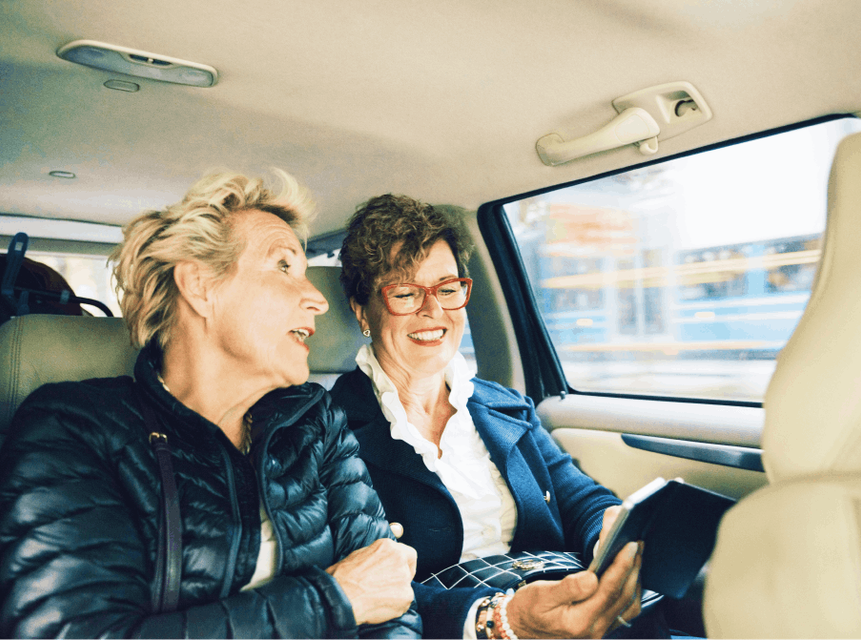 Two women traveling in the back of a car seeing the Tokyo sites. They are reading the Skyscanner Tokyo transport guide on their phone.