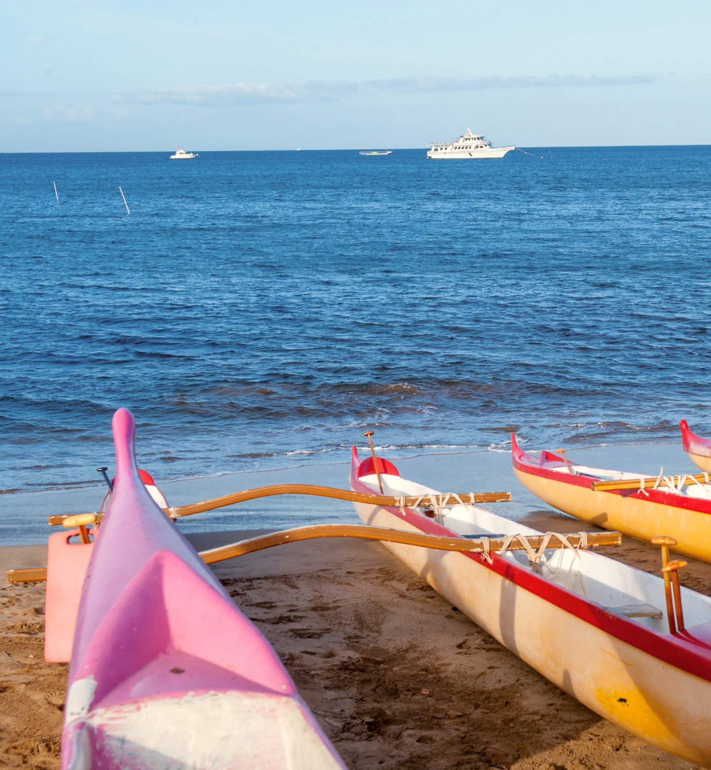 Colorful canoes rest on a sandy beach facing the open sea in Kahului, Maui.