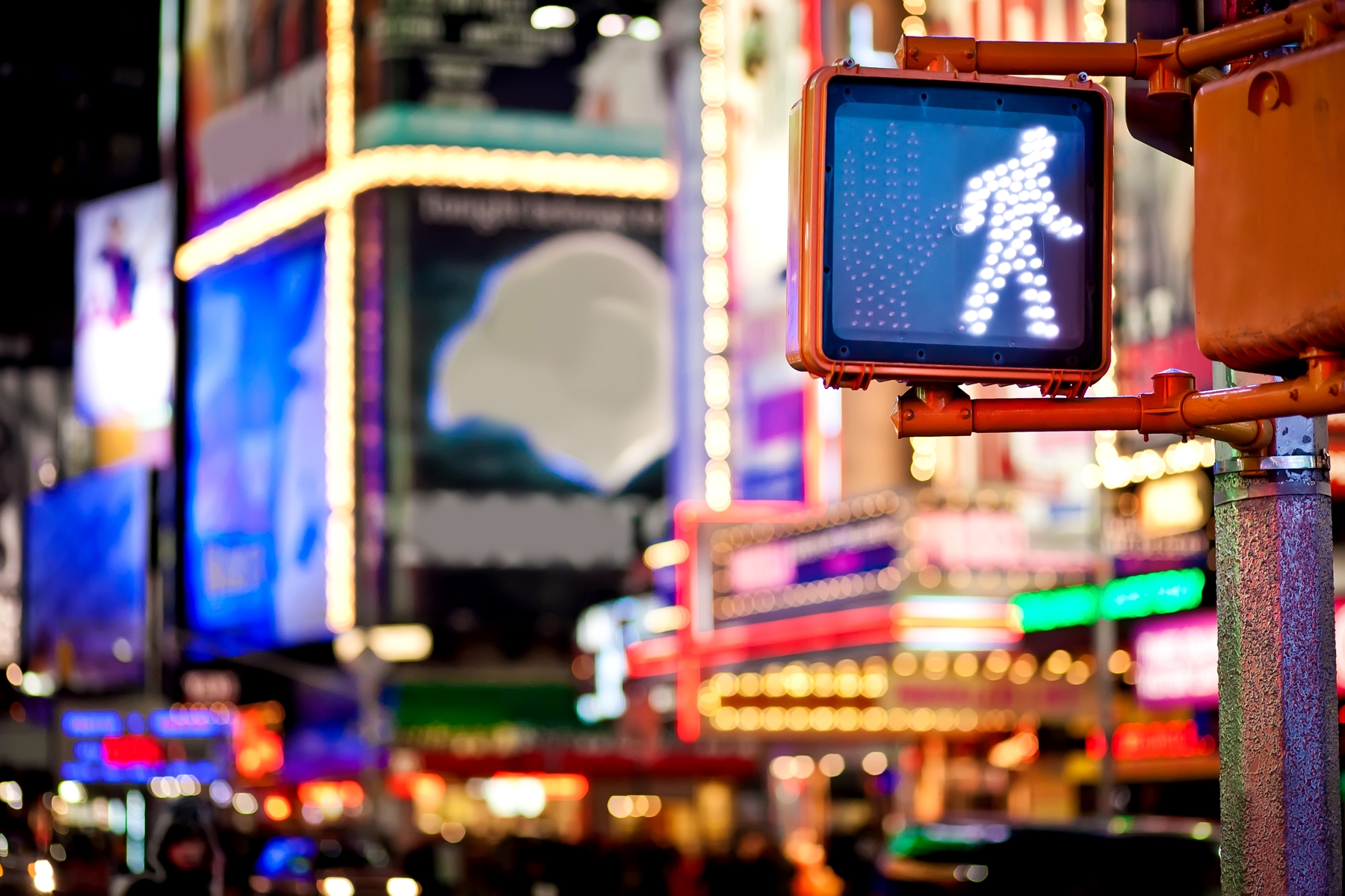 Focus on a pedestrian traffic light, with the bright lights of a big city blurred in the background.