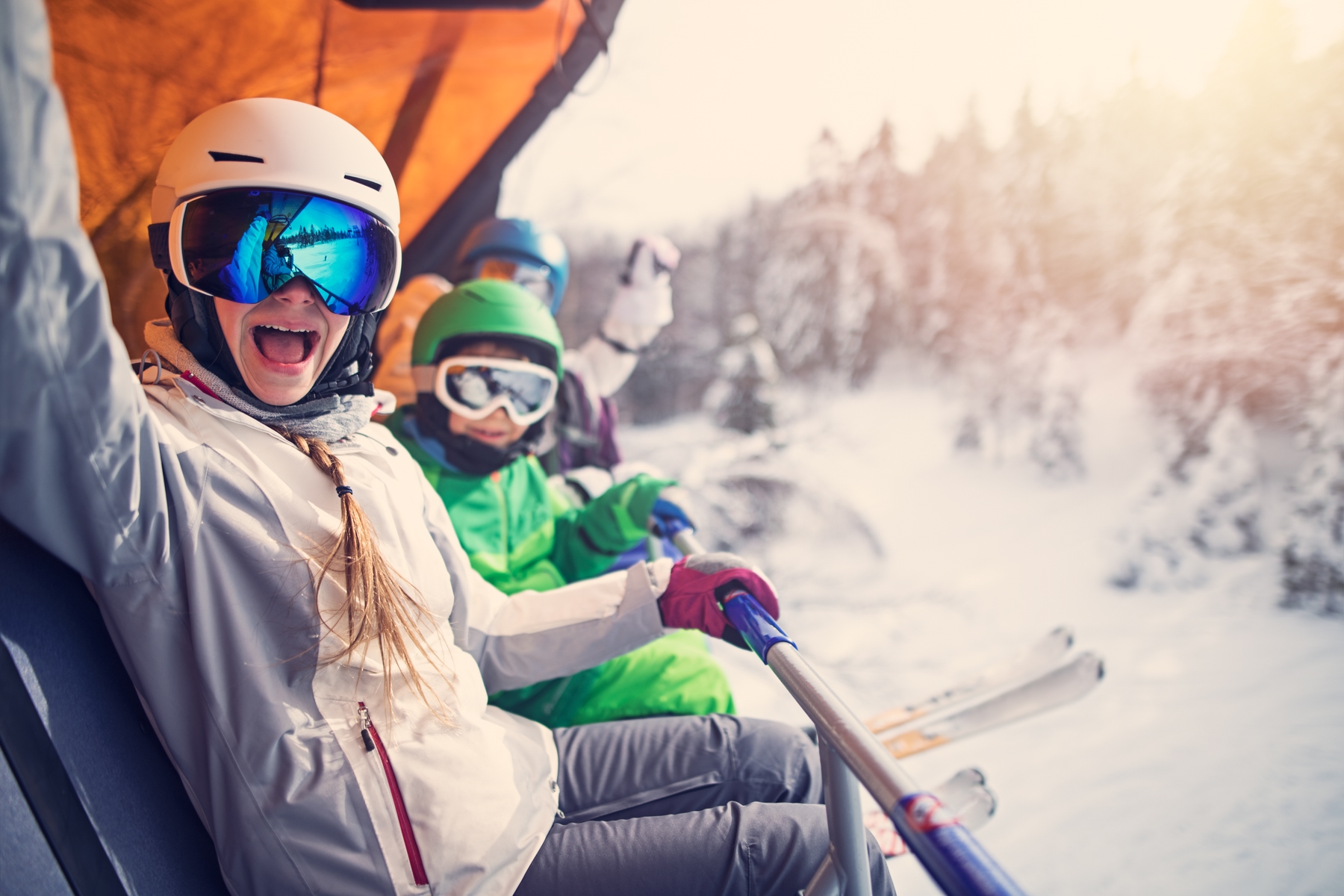 A family sitting on a ski lift and cheering at the camera, while the sun sets over an Alpine landscape