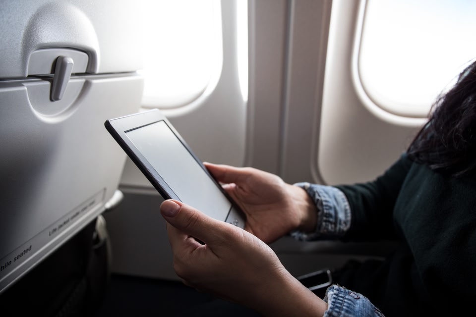 Vrouw met iPad in de hand voor raam in vliegtuig