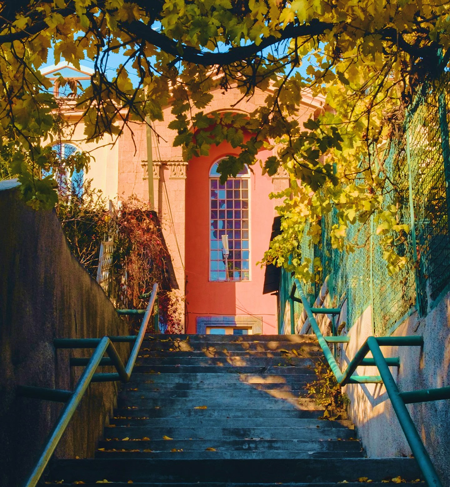 A salmon-pink building at the top of a staircase slightly obscured by trees in Yerevan, Armenia.