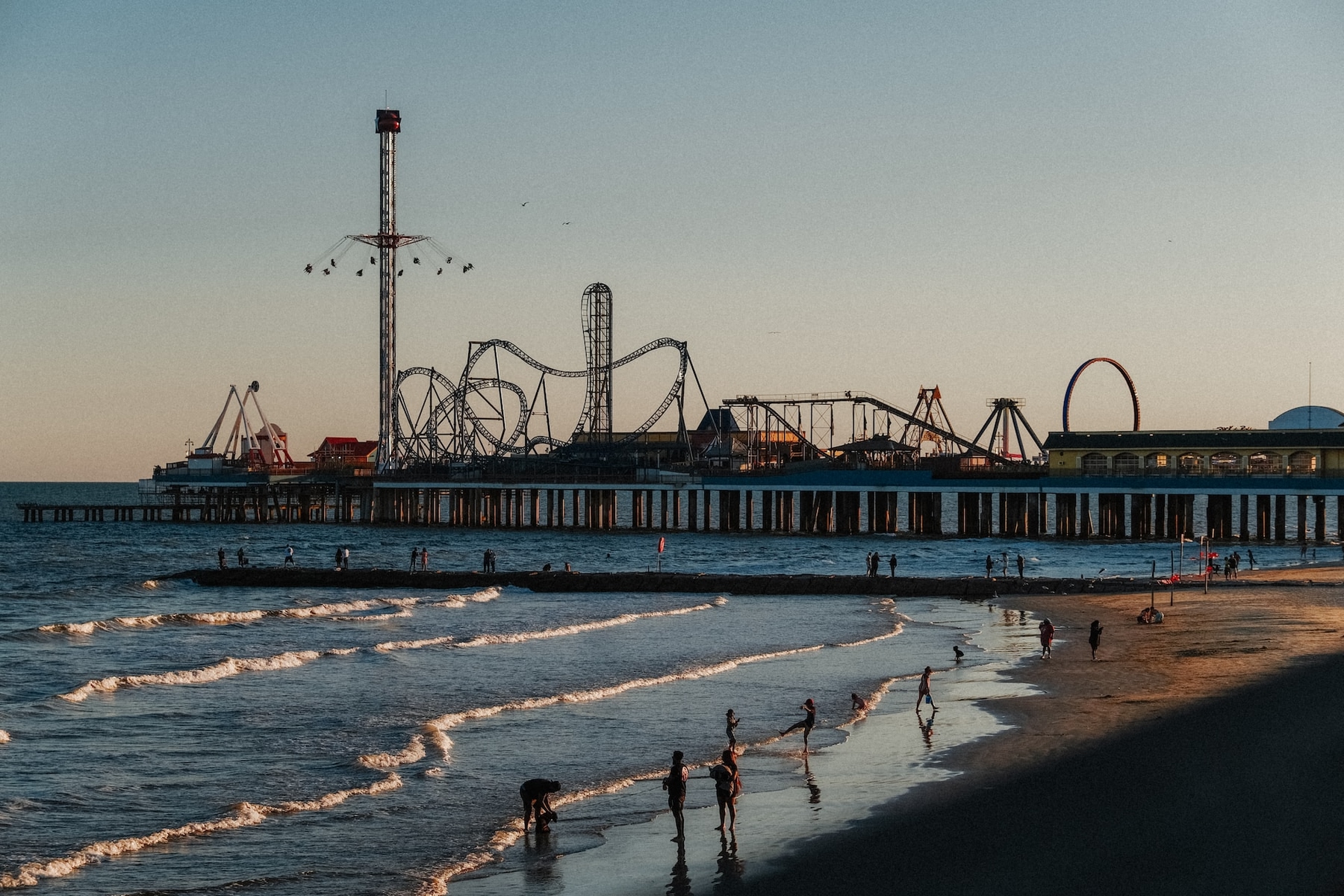 View of Galveston beach and swimmers, with Pleasure Pier  amusement park in the background.