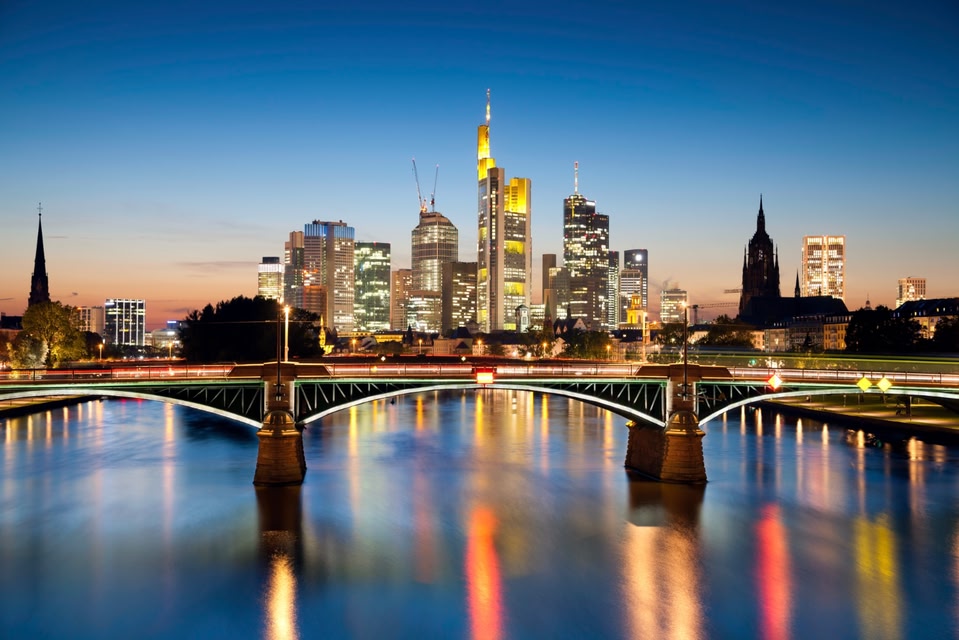 Frankfurt skyline at sunset, with lights reflecting on the river.