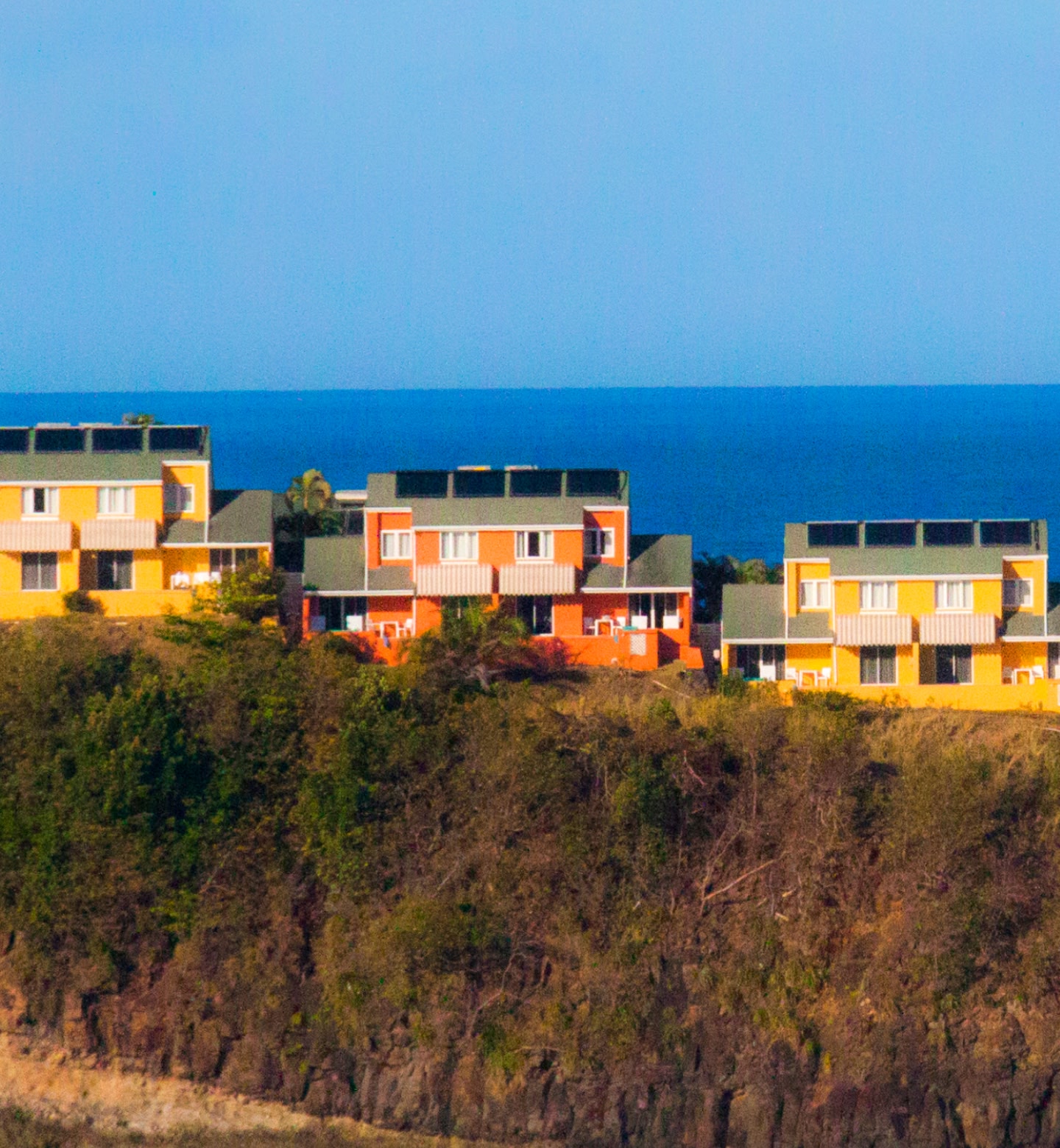 Three orange and yellow houses sit on a hillside with the sea in the background in Castries, Saint Lucia.