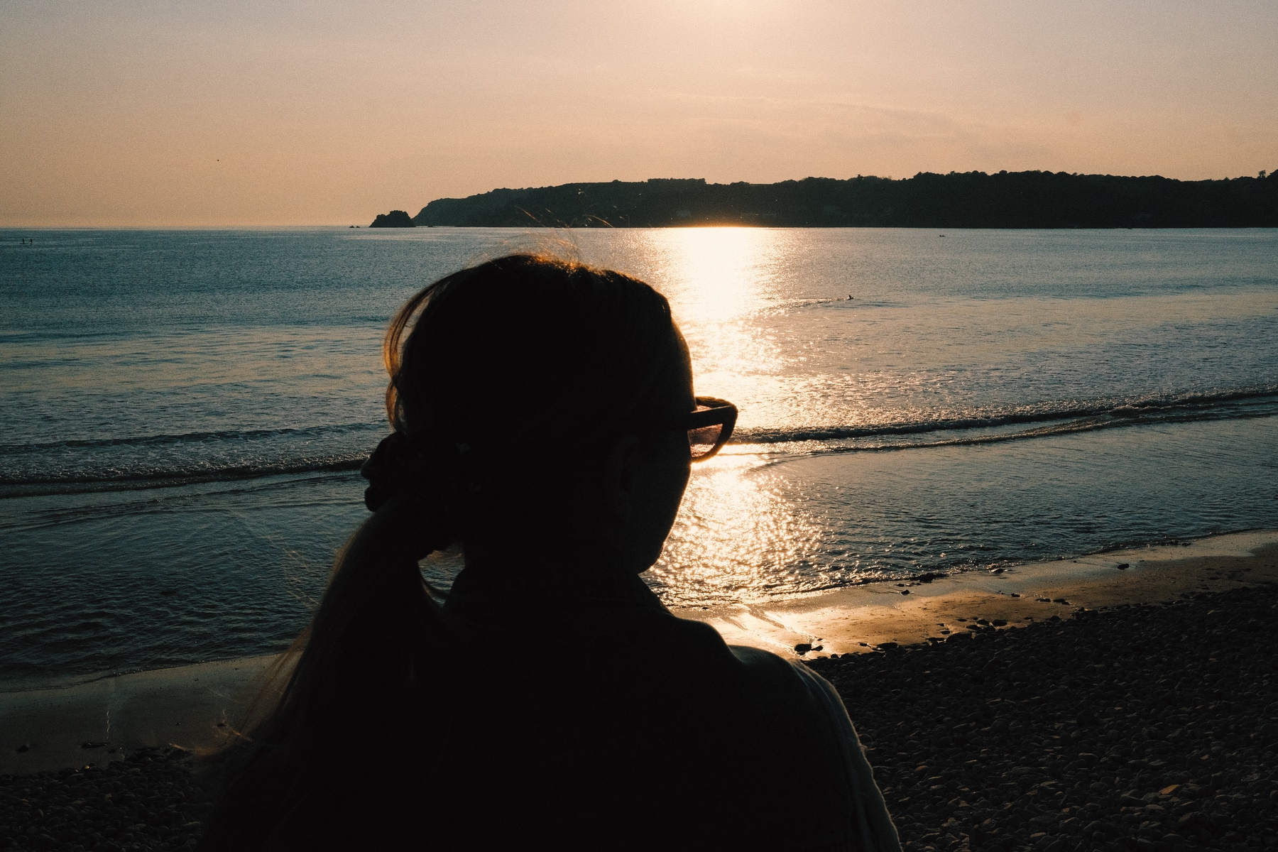 A woman looking out on a beach at sunset.
