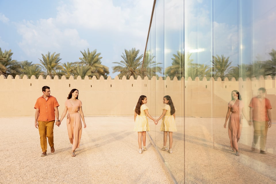 Un couple se tient la main tandis qu'une jeune fille regarde son reflet dans le mur de miroirs de Qasr Al Muwaiji, un fort du 20e siècle exprimant la culture d'Abu Dhabi.