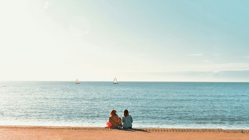 Zwei Frauen sitzen am Strand und scheuen aufs Meer hinaus
