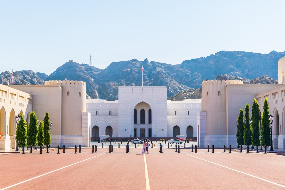 Un immeuble de carrure institutionnelle sert comme encadrement pour un square public avec les visiteurs qui le traversent. Derrière le bâtiment, des montagnes de lèvent vers un ciel bleu.