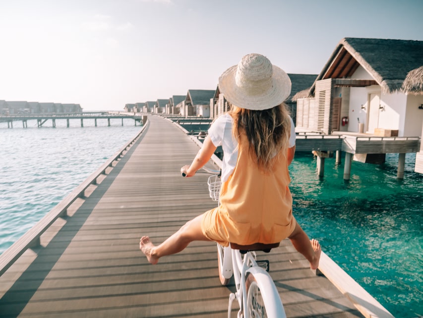 Mulher anda de bicicleta entre os bangalões nas Maldivas