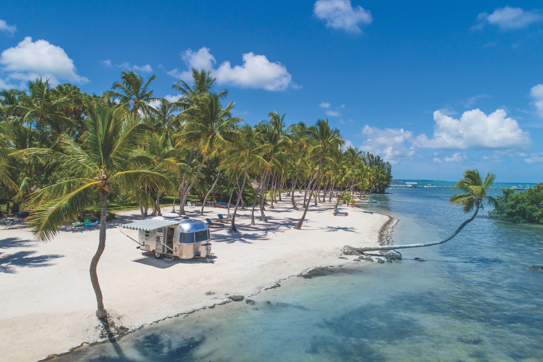blue water meeting white sand beach with a glamping resort airstream trailer