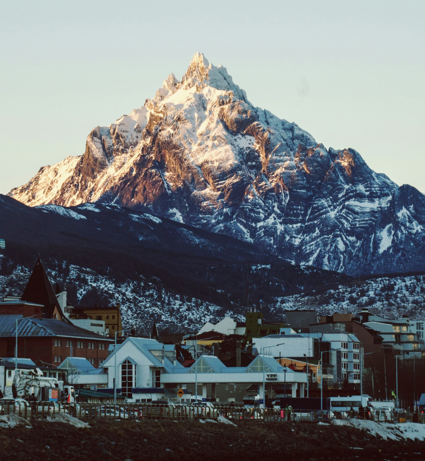 Uma montanha coberta de neve elevando-se sobre Ushuaia, Argentina, ao pôr do sol.