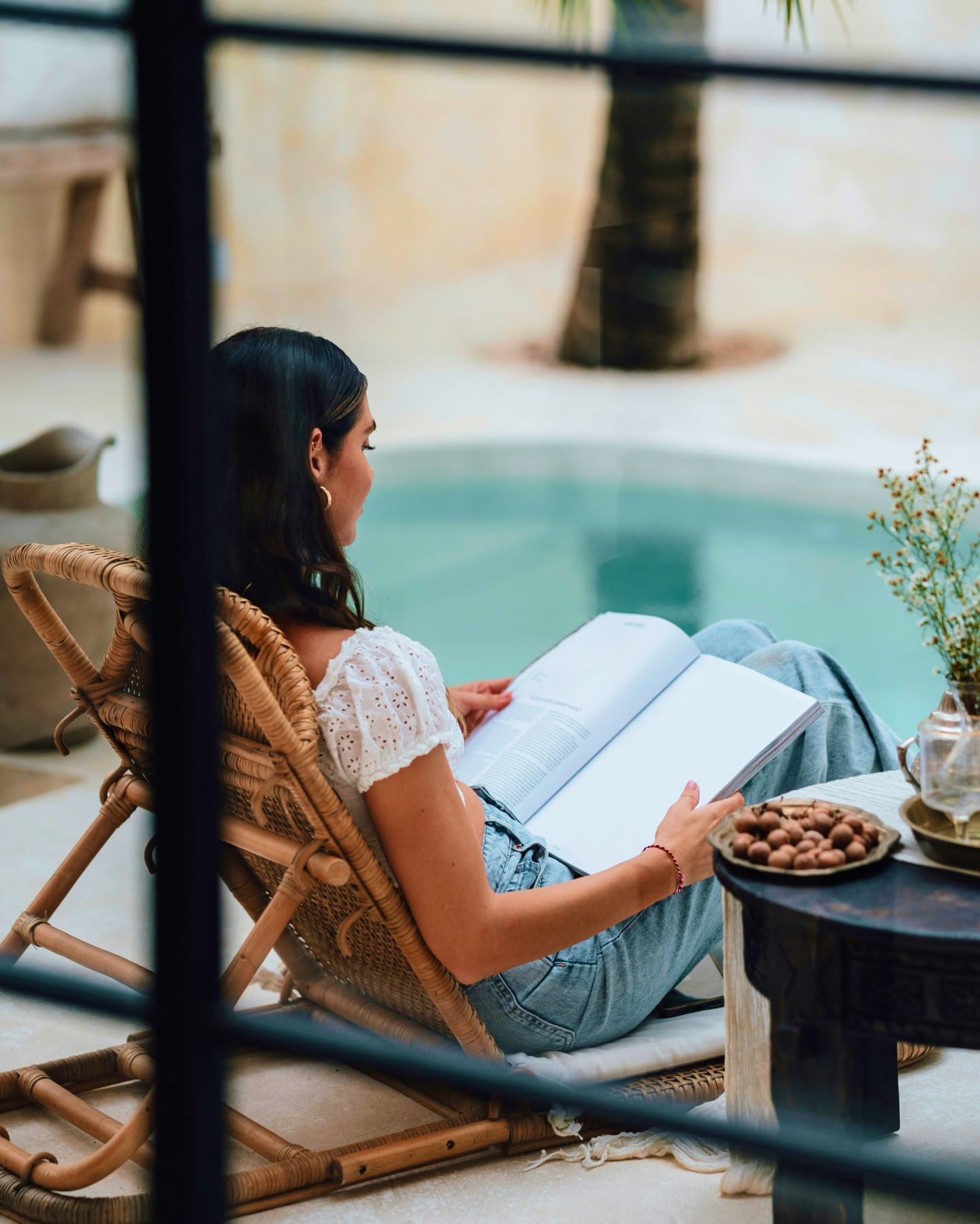 A young woman reclining by a pool, reading a large book