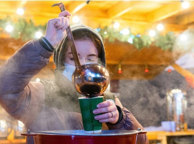 vrouw die glühwein serveert bij een kraam op de kerstmarkt