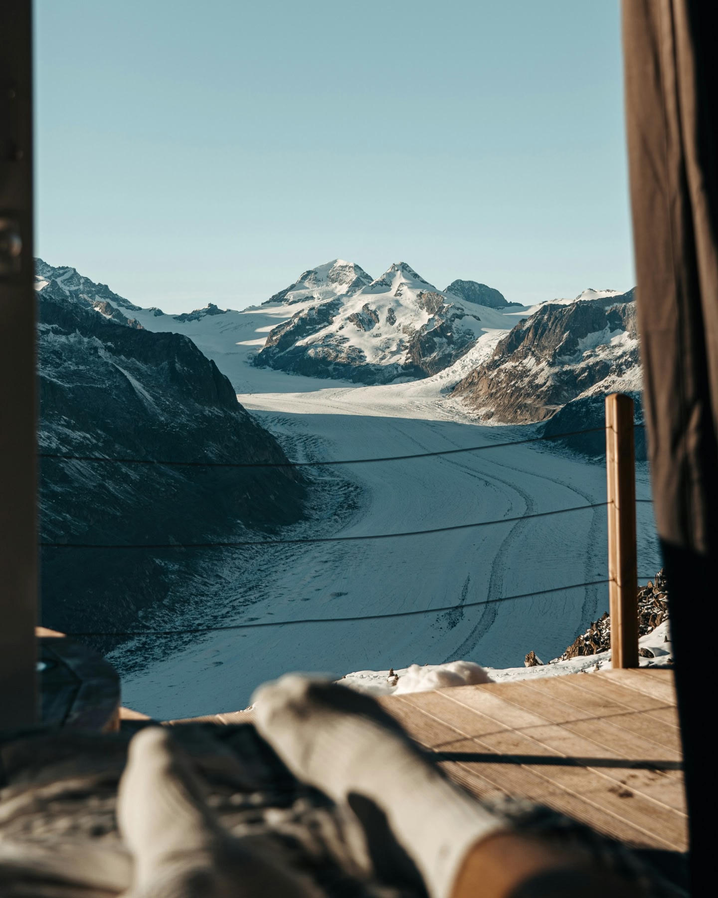 窓から見える山々の頂のあいだを走る雪道。前に靴下を履いた足元が見える。