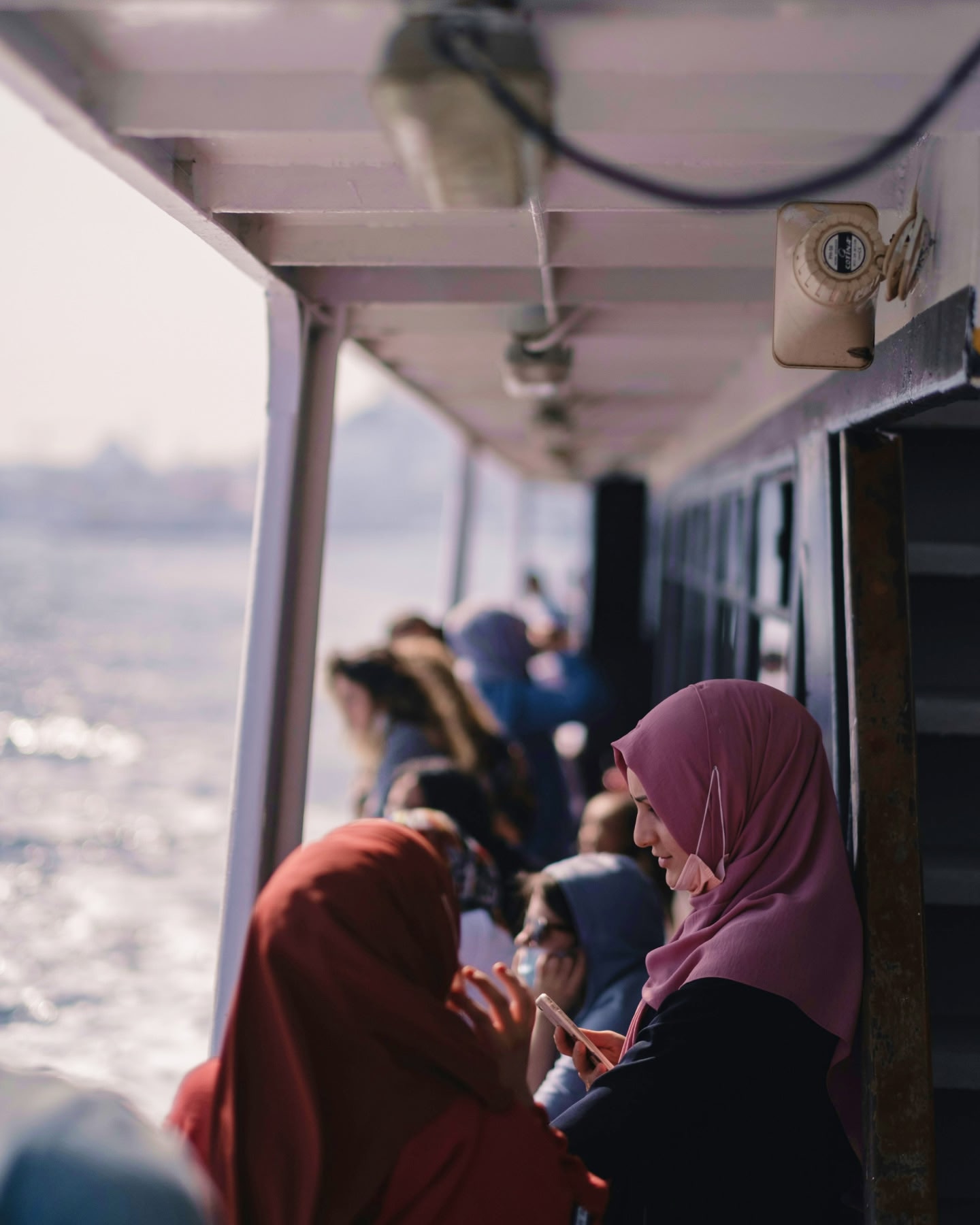 Two women wearing headscarves chat on a busy ferry.