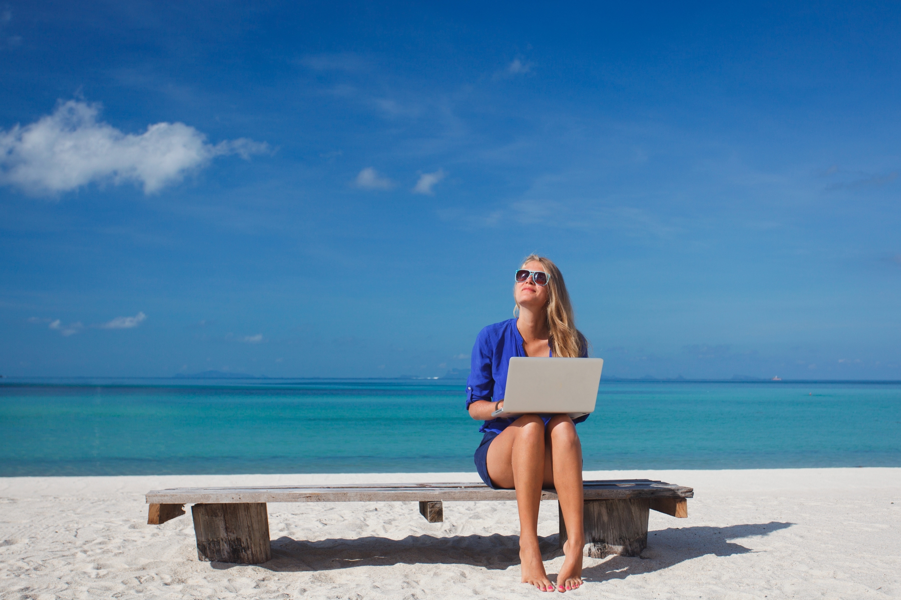 woman sitting on a bench on a sunny day at the beach alone with her laptop