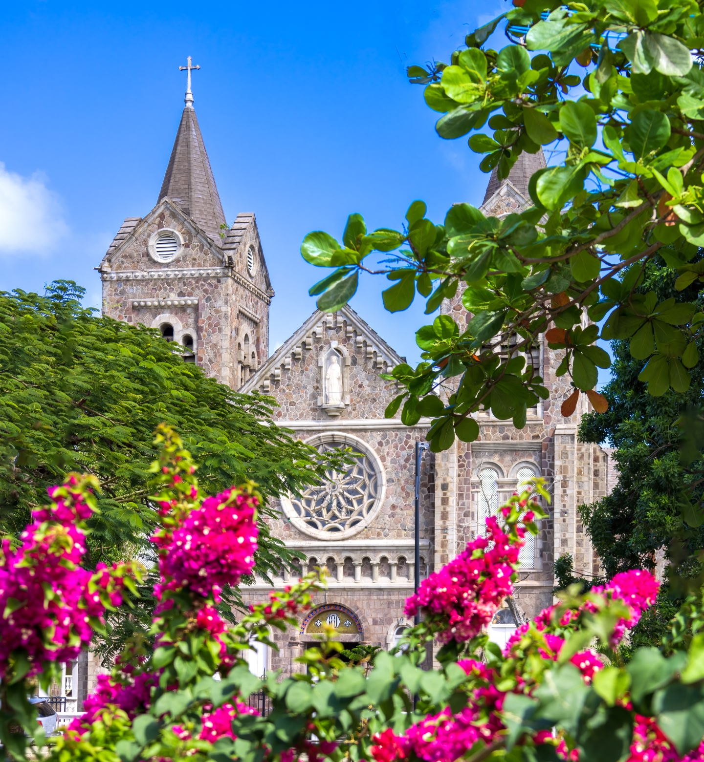 A traditional stone church sits beyond trees and flowers in the foreground in Basseterre, Saint Kitts.