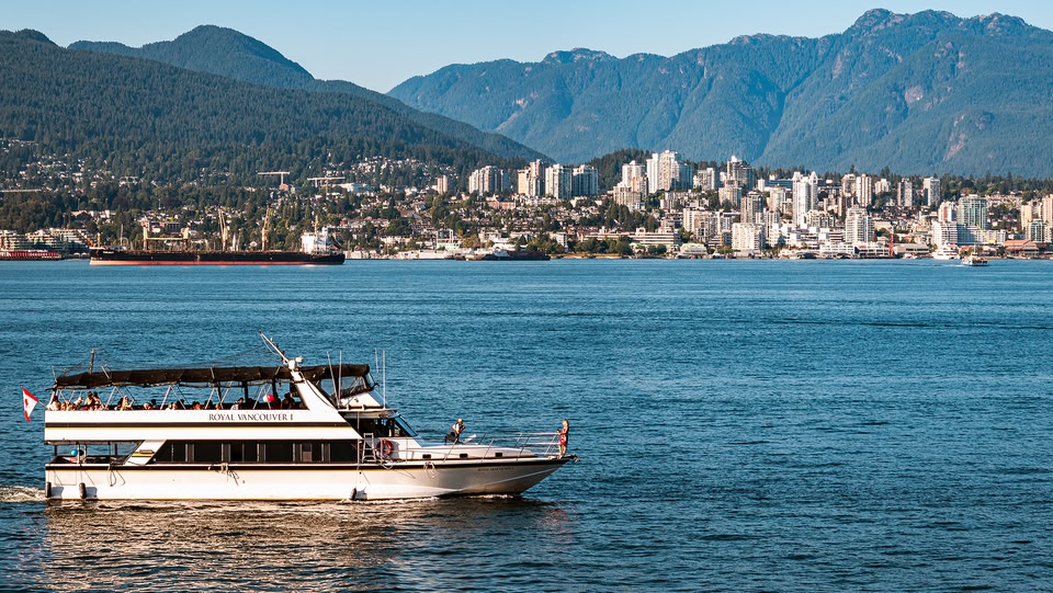 Scenic view of Vancouver, Canada, featuring a tour boat on the water with the city skyline and mountains in the background.