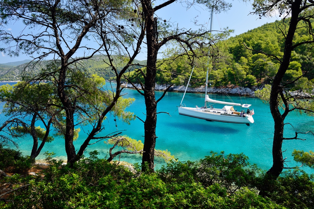 Yacht in calm turqoise waters, seen through lush green trees - Skopelos, Sporades Islands