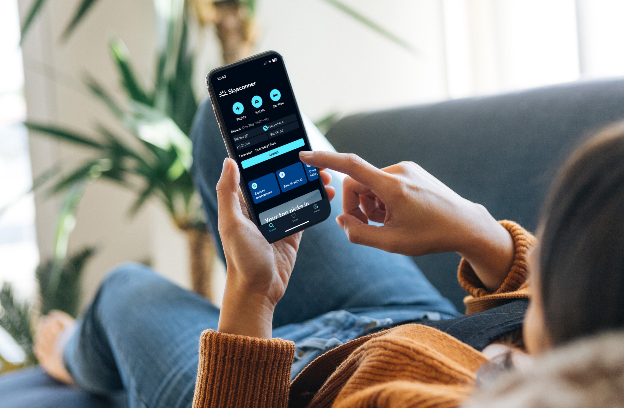 Person lying down on a sofa using the Skyscanner app to search for a flight.