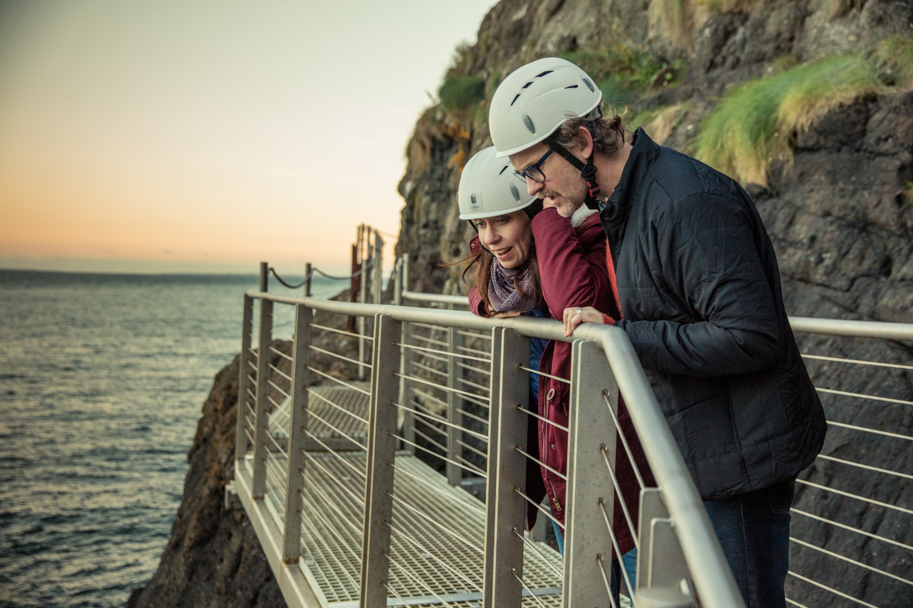 Woman and man standing on the Gobbins cliff path at sunset, marvelling at the sight of the Atlantic Ocean.