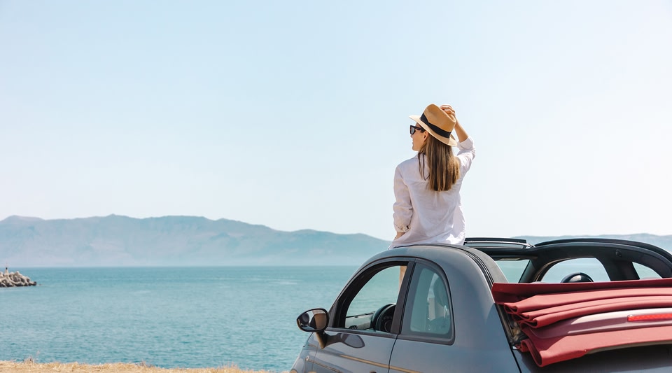 Person sitting on the hood of a car looking at a body of water.