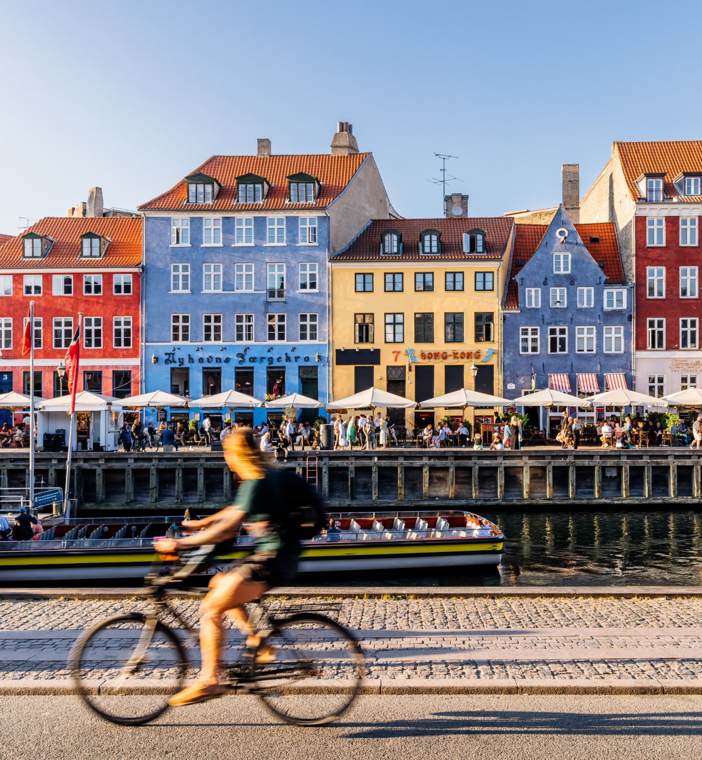A cyclist pedals past colourful houses and boats in Nyhavn Harbour, Copenhagen.
