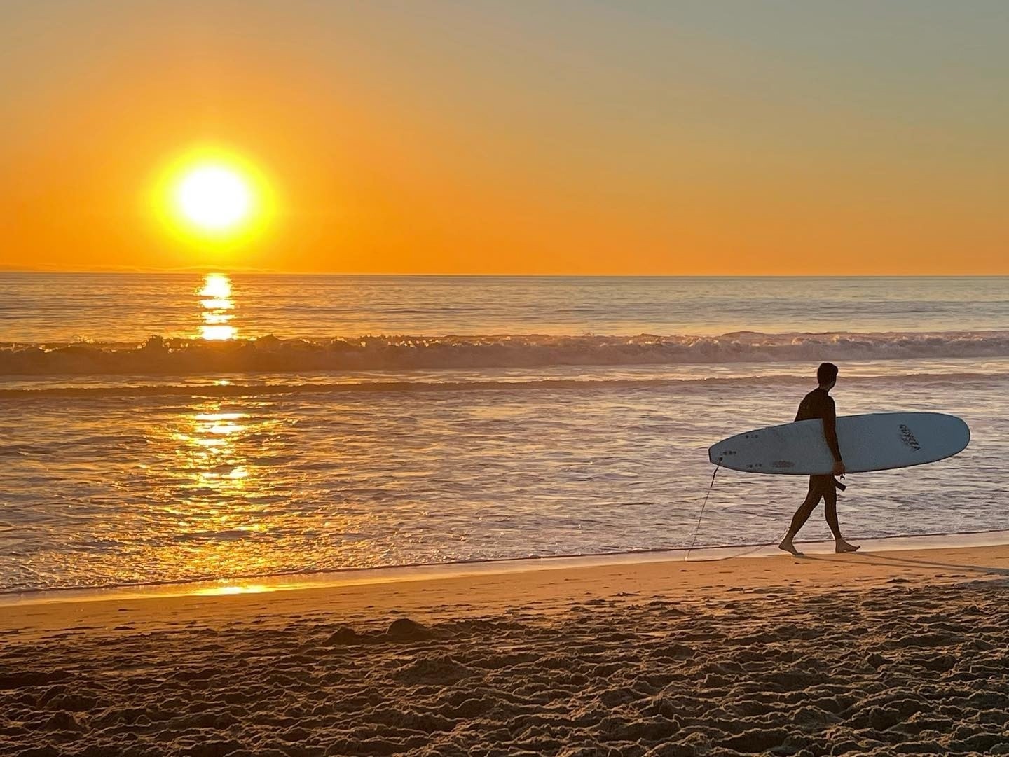 surfer on beach at sunset in Los Angeles, sun and Pacific Ocean.