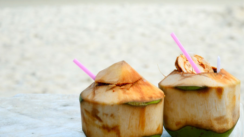 Two coconuts with straws sticking out of the top sitting on a table on the Playa Forum beach.