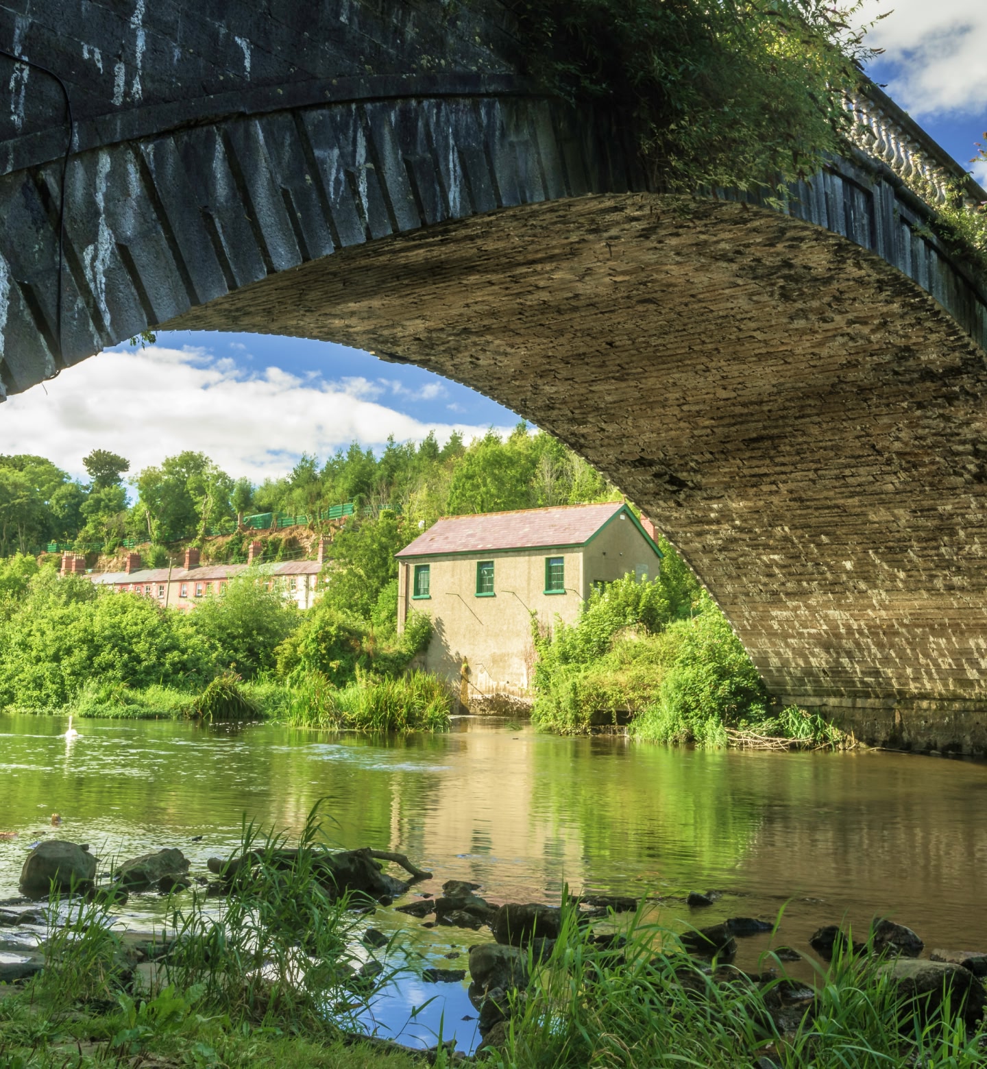 A sunny rural scene in Dublin, Ireland, showing a bridge crossing a river with housing in the background.