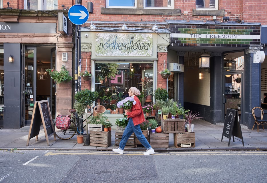 Woman holding bunch of flowers walking past Northern Flower, 58 Tib St, Manchester, England, UK.