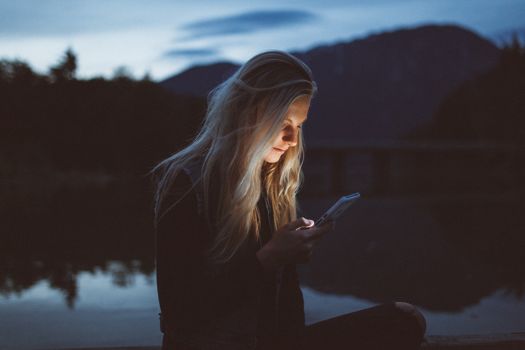 A young woman is checking her phone outdoors at night.